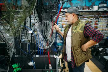 Happy fisherman choosing net in fishing shop, hooks and baubles on background. Equipment and tools for fish catching and hunting, accessory choice on showcase in store, bait assortment