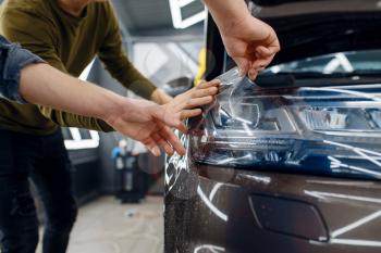 Workers applies car protection film on front fender. Installation of coating that protects the paint of automobile from scratches. New vehicle in garage, tuning procedure