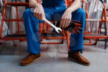 Male employee in uniform holds wrench in tool store. Choice of professional equipment in hardware shop, instrument supermarket