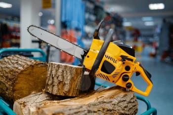 Chainsaw and wooden stump on showcase in power tool store closeup, nobody. Choice of equipment in hardware shop, electrical instrument in supermarket
