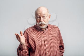 Bearded elderly man with mustache stands in a shirt, grey background. Mature senior looking at camera in studio