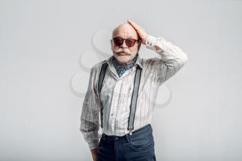 Bearded elderly man with mustache poses in sunglasses, grey background. Mature senior looking at camera