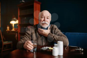 Elderly man takes pills in home office, age-related diseases. Mature senior is ill and being treated in his house