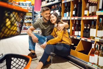 Cheerful couple with cart in grocery supermarket together. Man and woman buying beverages in market, customers shopping food and drinks