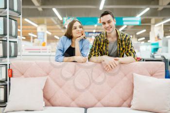 Young love couple poses at the pink couch in furniture store. Man and woman looking samples for bedroom in shop, husband and wife buys goods for modern home interior