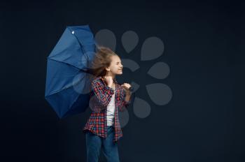 Little girl holds an umbrella in studio, wind effect, powerful airflow. Children with developing hairs, kids isolated on dark background, child emotion
