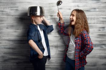 Little boy with a pot on his head and girl with the ladle in hand in studio. Children play, kids isolated on wooden background, child photo session