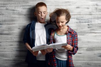 Little boy and girl are reding a book against powerful airflow in studio, developing hair, windy effect. Children and wind, kids isolated on wooden background, child emotion