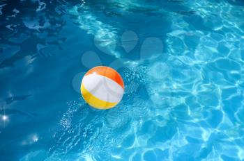 Colorful ball in blue water in the pool, nobody. Sports and entertainment at the poolside in sunny day, summer holidays, active lifestyle