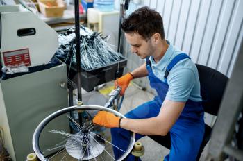 Worker with machine tool installs new bicycle spokes on factory. Bike wheels assembly in workshop, cycle parts installation