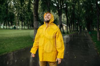 Man in raincoat enjoying the rain in summer park. Happy male person in rain cape on walking path, wet weather in alley
