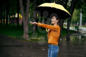 Woman with umbrella enjoys rain in summer park, rainy day. Female person walking alone, wet weather in alley