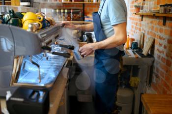 Male barista in apron prepares aroma coffee in cafe. Man makes fresh espresso in cafeteria