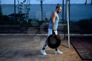 Muscular man carries barbell weights, street workout, crossfit. Fitness training on sports ground outdoor, male person pumps muscles, active urban lifestyle