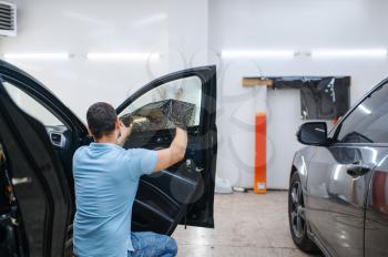 Male specialist installs wetted car tinting, tuning service. Mechanic applying vinyl tint on vehicle window in the garage