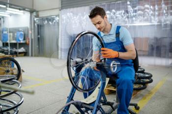 Male worker at the machine tool checks bicycle rim on factory. Bike wheels assembly in workshop