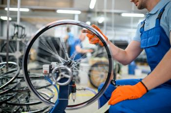 Male worker at the machine tool checks bicycle rim on factory. Bike wheels assembly in workshop, cycle parts installation