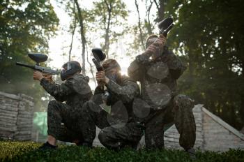 Paintball team in masks, battle on playground in the forest. Extreme sport with pneumatic weapon and paint bullets or markers, military game outdoors, fight tactics