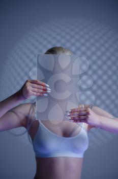 Futuristic young woman holds blur glass at her face, grey background. Female person in virtual reality style, future electronic technology, futurism concept