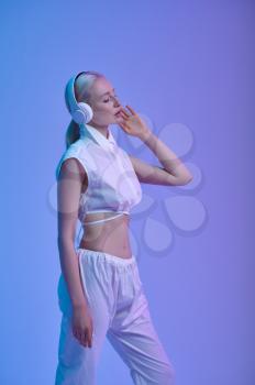 Attractive futuristic woman in white clothes and modern headphones, blue background. Sexy female person in virtual reality style, future technology, futurism