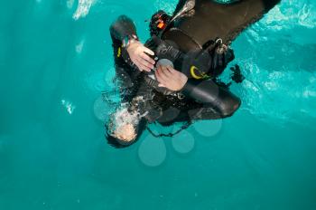 Male diver in scuba gear poses in pool, top view, course in diving school. Teaching people to swim underwater, indoor swimming. Man with aqualang