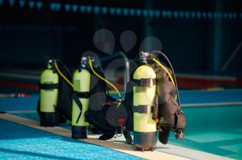 Three oxygen tanks at the poolside, scuba gear, aqualang, diving equipment. Teaching people to swim underwater, indoor swimming pool interior on background