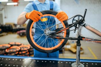 Bicycle factory, worker at assembly line, wheel installation. Male mechanic in uniform installs cycle parts in workshop, industrial manufacturing