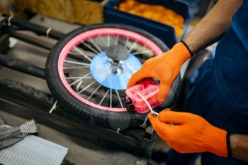 Bicycle factory, worker packs kid's bike. Male mechanic in uniform installs cycle parts, assembly line in workshop, industrial manufacturing