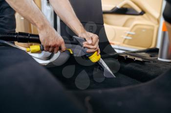 Worker cleans car interior with vacuum cleaner, car dry cleaning and detailing. Vehicle washing in garage