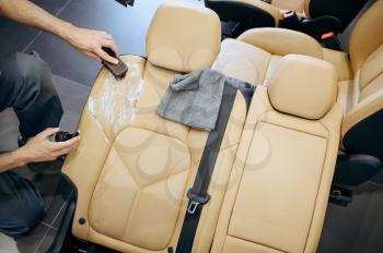 Worker with brush and spray wipes removed car seat, top view, dry cleaning and detailing. Vehicle washing in garage, thoroughly care of automobile, chemical and vacuum clean service