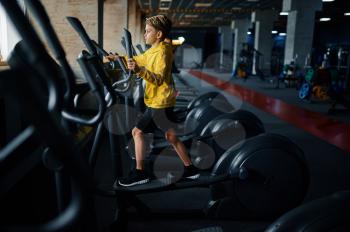 Child on exercise machine, side view, training in gym. Youngster in sport club, healthcare and healthy lifestyle, schoolboy on workout, sportive youth