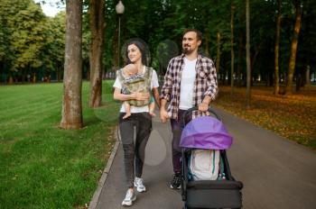 Happy parents with little baby walking by the sidewalk in summer park. Mom and dad leisures with male kid, picnic with child in the forest, family happiness