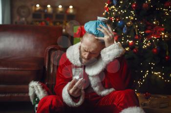 Vile Santa claus with hangover sitting on sofa, nasty party, humor. Unhealthy lifestyle, bearded man in holiday costume, new year and alcoholism