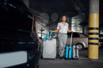 Happy woman with many suitcases in car parking. Female traveler with luggage in vehicle park lot, passenger with bag. Girl with baggage near automobile