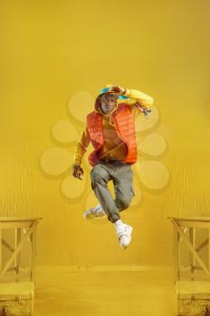 Young rapper jumps in studio with yellow tones. Hip-hop performer, rap singer, break-dance performing, entertainment lifestyle