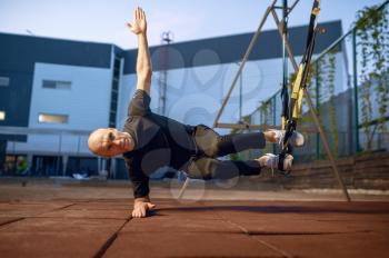 Sportive man doing balance exercise with ropes on sports ground outdoors. Slim female person in sportswear, outside fitness training, fit workout