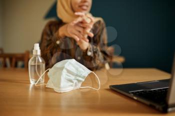 Medical mask and antiseptic, arab girl in hijab in university cafe on background. Muslim woman with books sitting in library. Religion and education