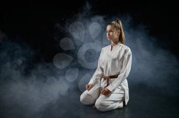 Female karateka on training in white kimono sitting on the floor, dark background. Karate fighters on workout, martial arts, women fighting competition