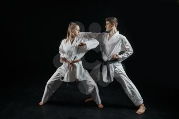 Female karate fighter on training with master, white kimono, dark smoky background. Karateka on workout, martial arts, fighting