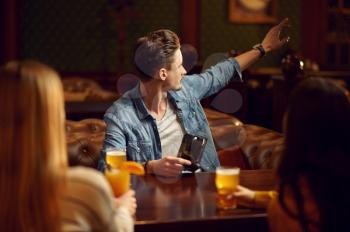Male and female friends drinks alcohol at the table in bar. Group of people relax in pub, night lifestyle, friendship, event celebration