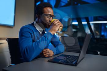One manager in glasses works on laptop in night office. Male worker, dark business center interior on background, modern workplace