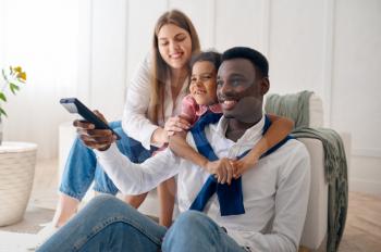 Happy family watching TV in living room. Mother, father and their daughter poses at home together, good relationship