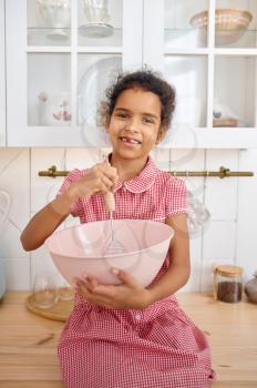 Funny little girl cooking the dough, nice breakfast. Smiling female child on kitchen in the morning. Happy childhood, young cook