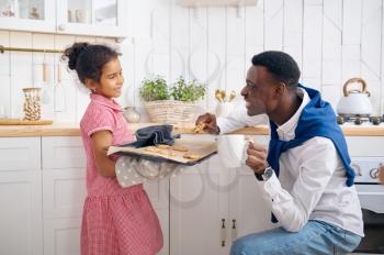 Happy father and daughter eats fresh cakes on breakfast. Smiling family eats on the kitchen in the morning. Dad feeds female child, good relationship