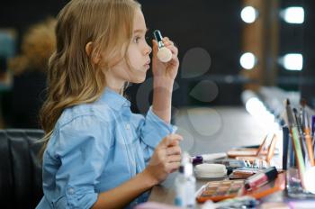Little girl applies powder at the mirror in makeup salon. Mom and daughter play stylists together, happy childhood, glamour family, young make-up artist or hairdresser