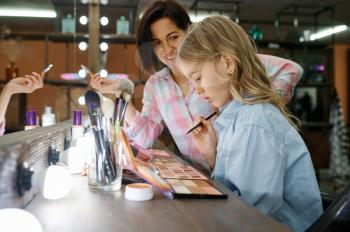 Mother and daughter using shadow palette in makeup salon. Mom and little girl play stylists together, happy childhood, glamour family