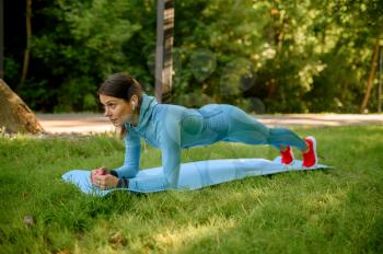 Morning fitness training on mat in park, woman in headphones. Female runner goes in for sports at sunny day, healthy lifestyle, jogger on outdoors workout