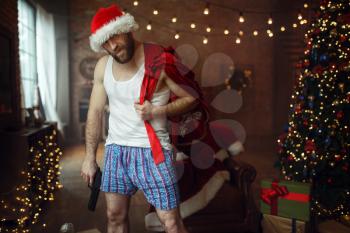 Bad Santa claus gangster with gift bag and gun, nasty party, humor. Unhealthy lifestyle, bearded man in holiday costume, new year and alcoholism