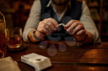 Man breaks a cigarette, bad habit and addiction, alcohol beverage on the table, vintage office interior on background. Tobacco smoking culture, specific flavor