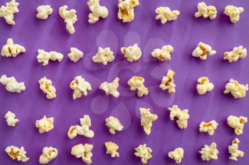 Popcorn pattern isolated on purple background, top view. Pop corn texture, tasty wallpaper design, movie or cinema food concept